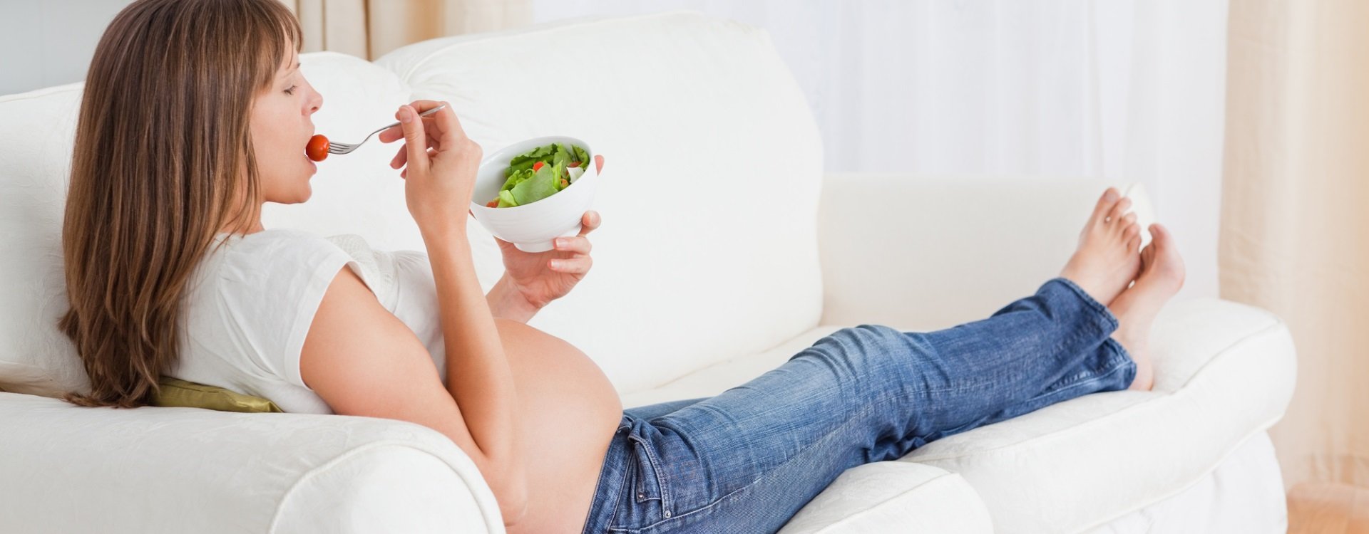 Schwangere, die auf dem Sofa liegt und Salat isst